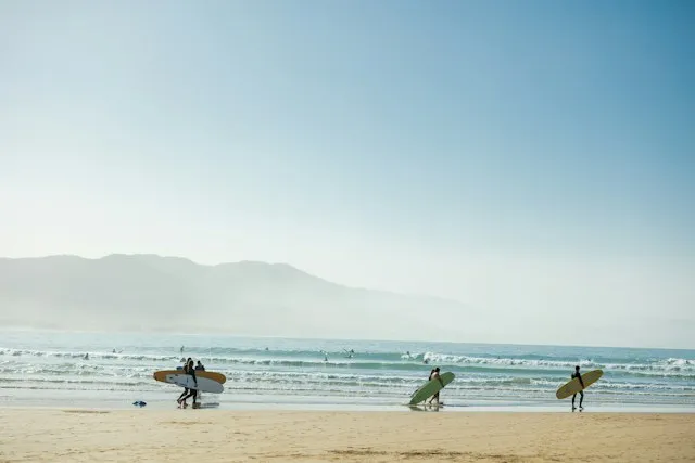 Surfers carrying boards across the beach at Imsouane Bay with mountains behind