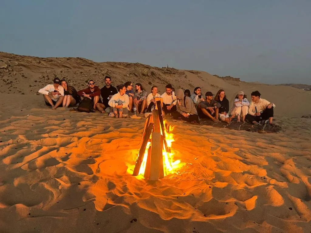 Camp crew gathered around an evening beach fire after surf — Private Week buyout