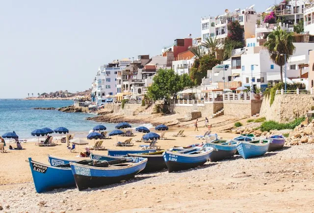 Fishing boats on Taghazout village beach beside waterfront buildings and beach umbrellas