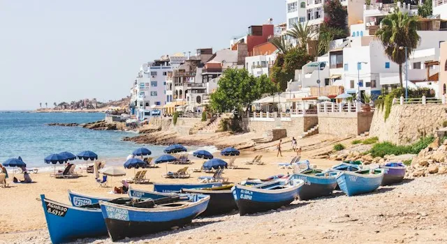 Fishing boats on Taghazout village beach beside waterfront buildings and beach umbrellas