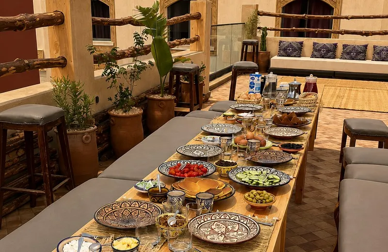 A long breakfast table laid on the terrace at our Tamraght house with bread, tomatoes, cucumber, olives, jam, eggs and tea