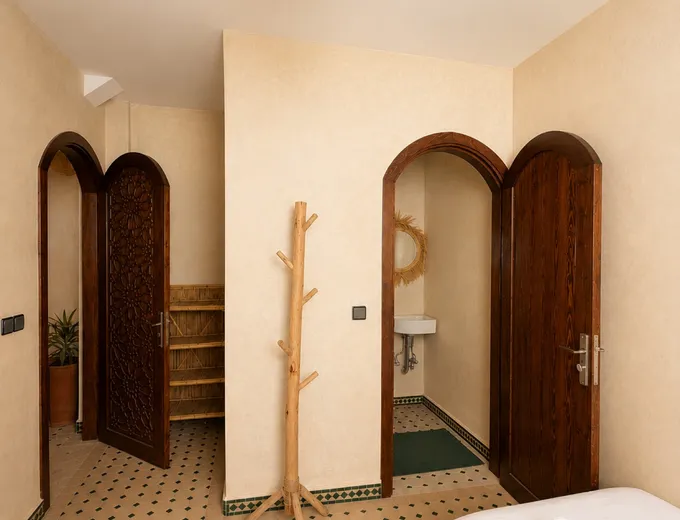 A twin room at the Kymata base in Tamraght: two single beds with towels, Moroccan tiled floor and an ensuite washroom through a carved arch