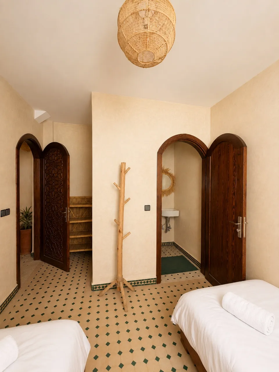 A twin room at the Kymata base in Tamraght: two single beds with towels, Moroccan tiled floor and an ensuite washroom through a carved arch